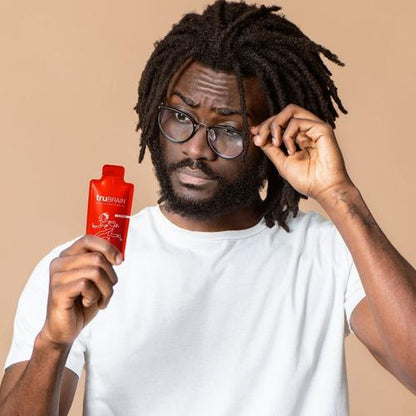 Creative professional man with curly hair holding up the 1oz TruBrain nootropic drink next to his head while gazing at its allure